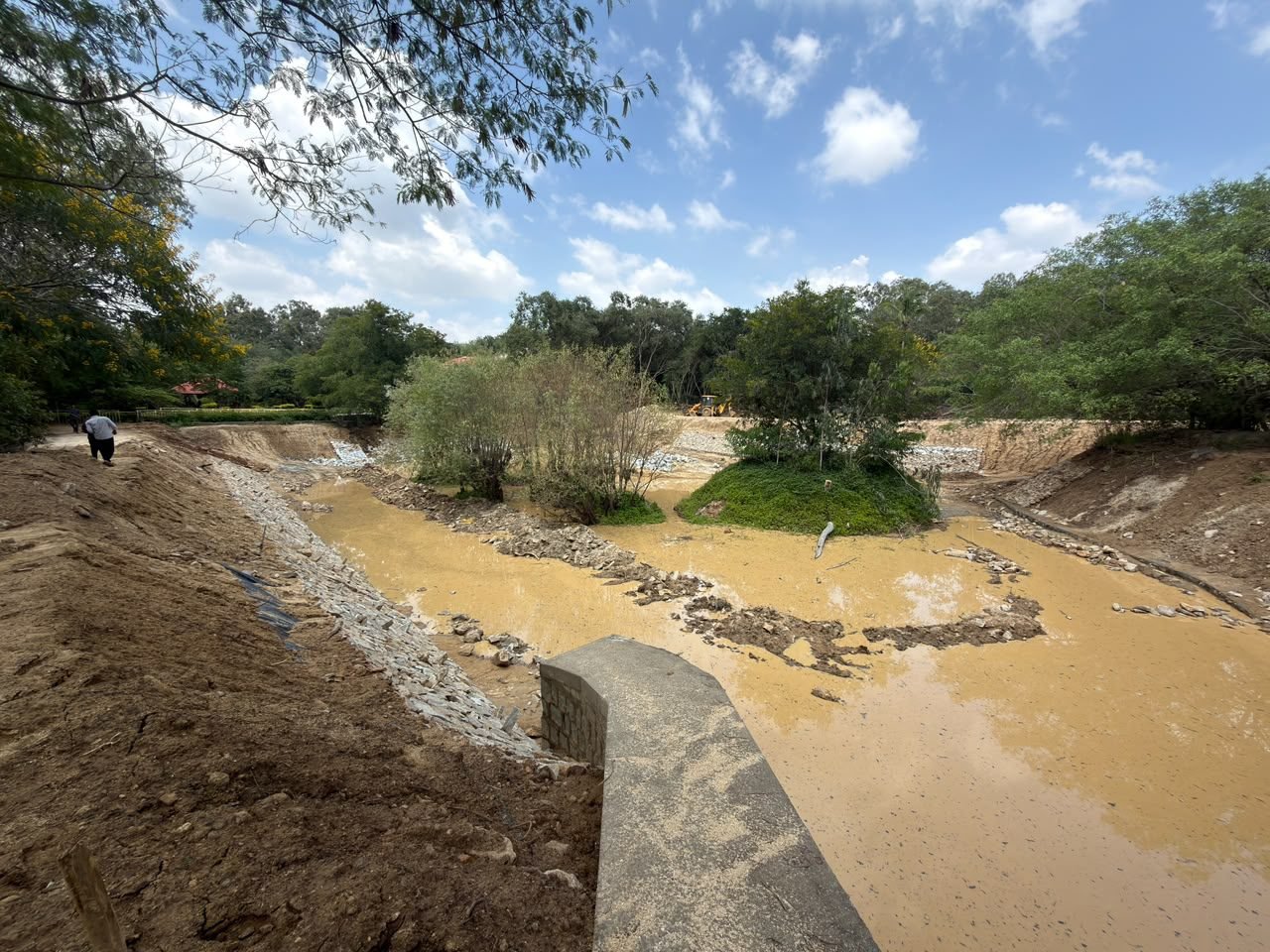 Lake with a vegetated island, stone-lined bank and a concrete structure in the foreground